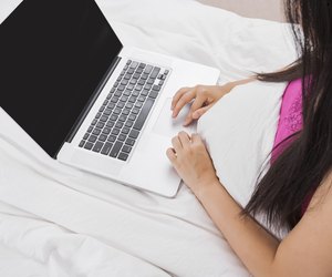 Midsection of woman using laptop on bed