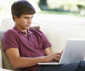 Teenage Boy Relaxing On Sofa At Home Using Laptop