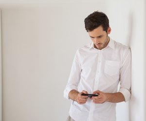 Casual businessman leaning against wall sending a text