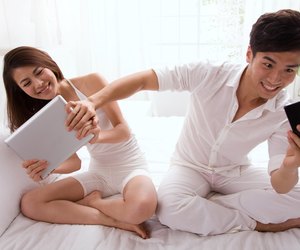 Young couple watching cell phone and tablet computer on bed
