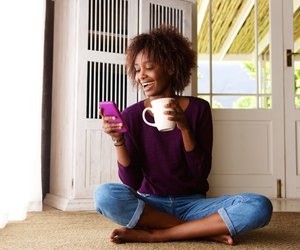 Smiling woman sitting on floor at home with cell phone