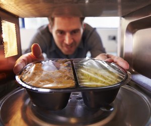Man Putting TV Dinner Into Microwave Oven To Cook