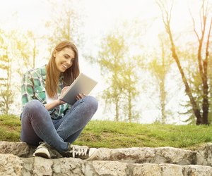 Happy young woman with digital tablet sitting in park