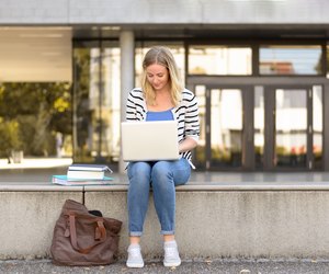Young female student sitting outside using laptop