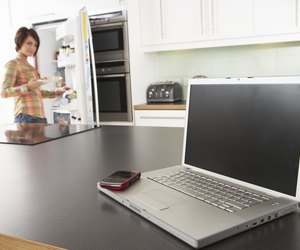 Young Woman Fixing Snack In Kitchen With Laptop In Modern Kitchen