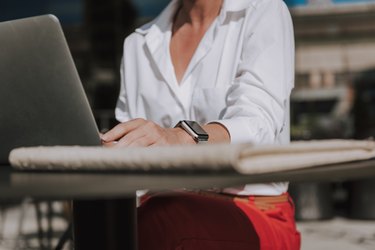 Cropped photo of businesswoman wearing white blouse and working at laptop
