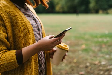 A red-haired woman is walking in the park and holding a bamboo cup with hot coffee