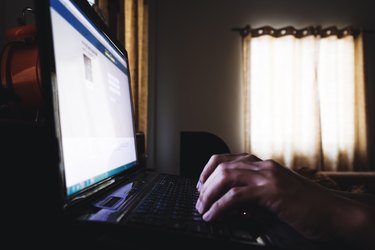 Hand typing laptop computer keypad, in dark room, selective focus