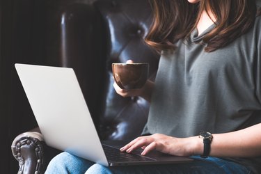 Closeup image of a woman working , using and typing on laptop keyboard while drinking coffee