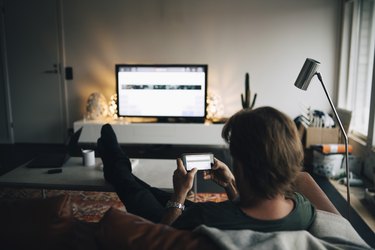 Full length of man using mobile phone while sitting on sofa in living room