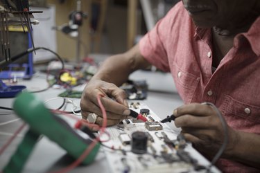 Close up male engineer using soldering iron on electronics