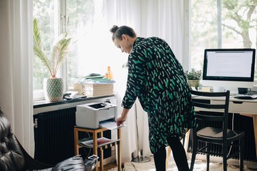 Young businesswoman using computer printer at home office