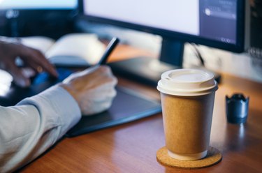 Desktop with computer, graphics tablet and a cup of coffee. Side view.