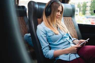 woman in headphones sleeping and listening music with smartphone during trip on travel bus