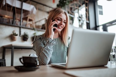 Elegant young woman talking on the phone and using laptop. Low angle view.