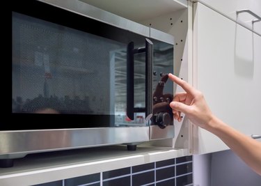 Woman's Hands pressing button on black microwave for cooking