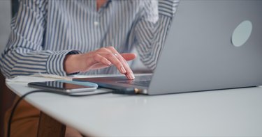 Close-up hand of young beautiful business woman working with laptop touch bar at light modern minimalistic office table.