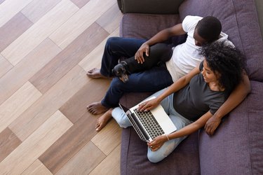 Happy african couple using computer sitting on sofa with pet