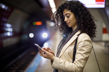 Young businesswoman standing on the subway station and using her mobile phone while waiting for the train
