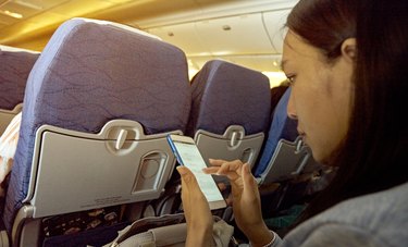 Side View Of Mid Adult Woman Using Mobile Phone While Sitting In Airplane