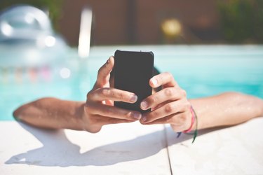 Close-Up Of Hand Holding Mobile Phone In Swimming Pool