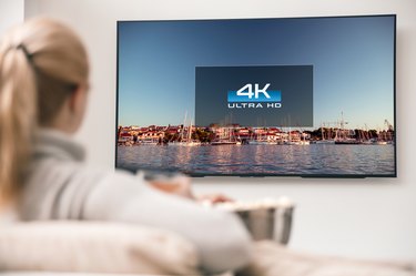 Big modern TV with 4k resolutions and young woman on foreground watching some video