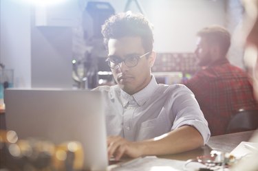 Serious, focused young male designer working at laptop in workshop