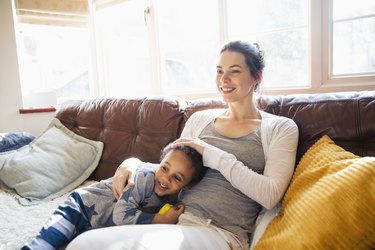 Affectionate mother and toddler son cuddling on living room sofa