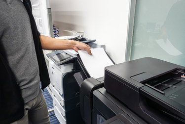 businessman put paper sheet into office printer tray for printing documents