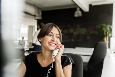 Cheerful businesswoman using telephone in office