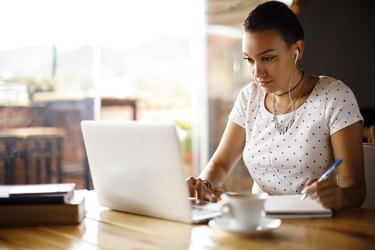 Attractive young woman working on laptop and taking notes at a cafe