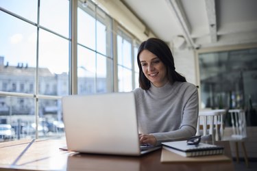 Smiling attractive female freelancer doing remote job using laptop computer