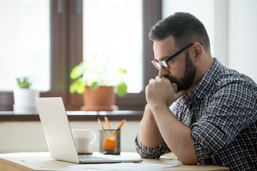 Millennial casual businessman thinking and looking at laptop in office