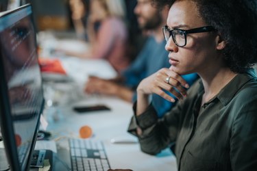 Concentrated African American woman brainstorming while coding data on desktop PC.