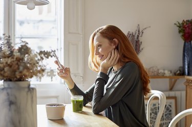 Smiling woman using phone while having breakfast