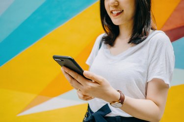 Portrait of smiling young woman using smartphone against colourful background in city