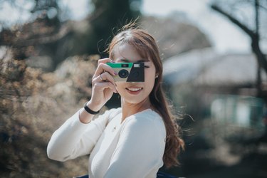 Joyful young woman taking photos with disposable camera in park on a lovely sunny day