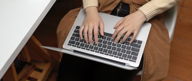 Female hands typing on laptop on her lap while sitting on office chair in office room