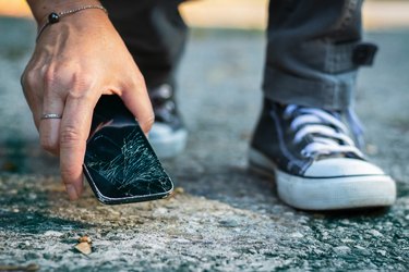 Woman picking up broken smartphone from the ground.