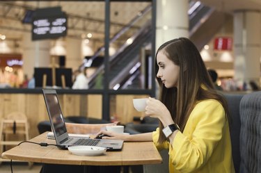 Young female freelancer drinking a cup of coffee in a cafe and working with her computer. Busy creative  entrepreneur having breakfast