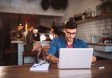 Young hipster businessman working on laptop at urban coffee shop