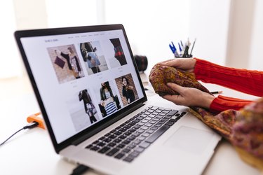 Close-up of fashion designer in studio with laptop examining fabric