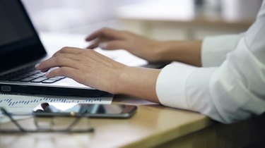 Hands of female office employee typing on laptop, enters survey data, closeup