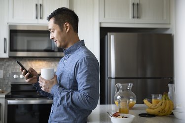 Man drinking coffee and using smart phone in morning kitchen