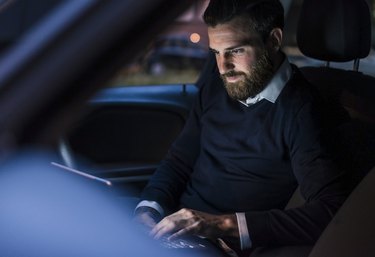 Businessman using laptop in car at night