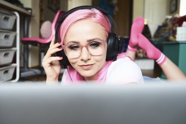 Young woman with pink hair listening to music via laptop at home