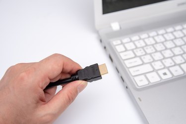 Man is connecting black hdmi cable into laptop.