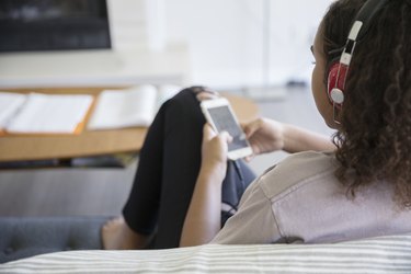 Teenage girl listening to music with headphones and mp3 player on living room sofa