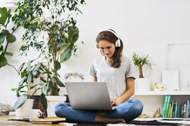 Young woman at home sitting on the floor using laptop and listening to music