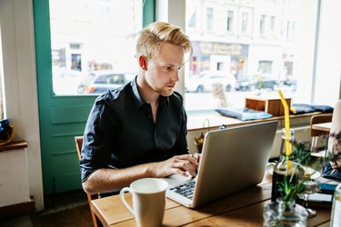 Young Man Working On Laptop In Cafe